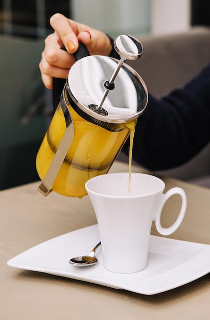 Una mujer vierte té de espino amarillo de una tetera en una taza