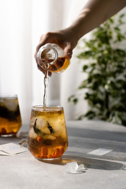 Una mujer vierte té helado de una botella en un vaso de hielo junto a una ventana soleada