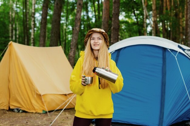 Una mujer en vierte té de un termo en una caminata Mañana en el bosque Vacaciones de verano