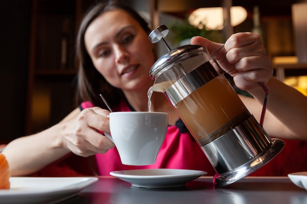 Mujer vierte té de una tetera en una taza