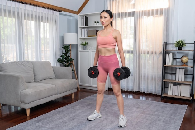Mujer vigorosa y enérgica haciendo ejercicio de levantamiento de pesas con mancuernas en casa Joven atlética mujer asiática sesión de entrenamiento de fuerza y resistencia como rutina de ejercicios en casa