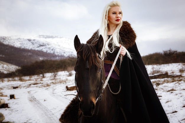 Mujer vikinga con un caballo negro contra el fondo de las montañas