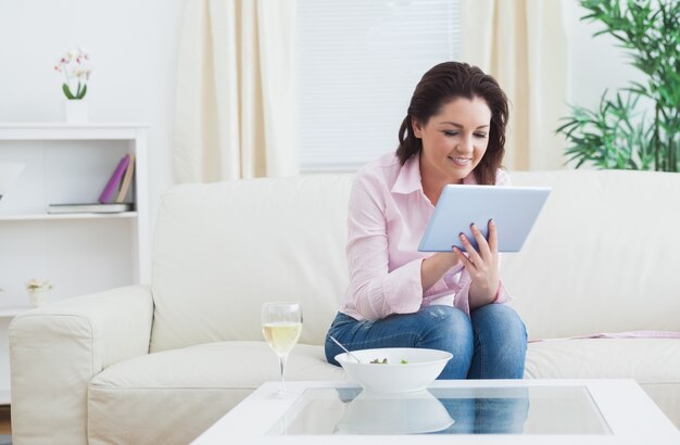 Mujer con vino y tazón con tableta digital en el sofá