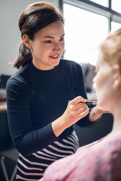 Mujer visagist aplicando cosmético de maquillaje a la mujer embarazada preparándose maquilladora trabajando