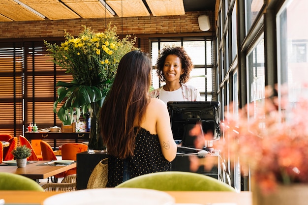 Foto mujer de la vista posterior que se coloca delante del cajero de sexo femenino joven que actúa en el escritorio de efectivo en café