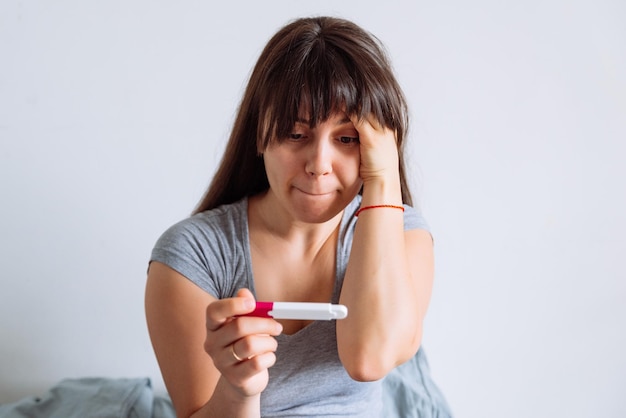 Mujer con vista preocupada mirando la prueba de embarazo mientras está sentada en la cama