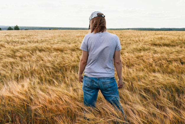 Mujer de vista trasera en jeans entre campo de trigo de cereal seco amarillo agricultura y cosecha de granos Amigable con la maqueta