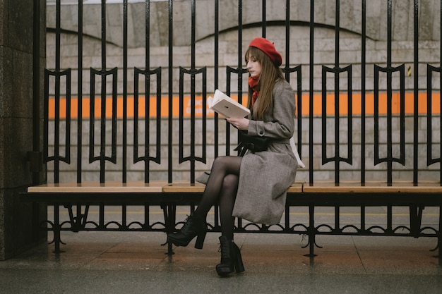 Mujer vistiendo abrigo boina y bufanda sentada sola en la estación de metro de San Petersburgo reding un libro