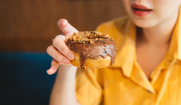 Mujer vistiendo camisa amarilla sosteniendo y mostrando una cobertura de donas caseras glaseadas de chocolate con aplastamiento de avellana.