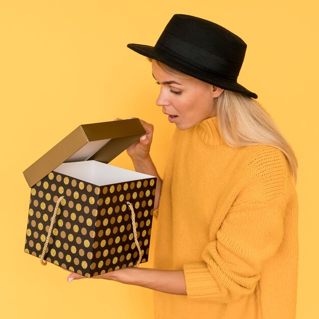 Mujer vistiendo camiseta amarilla mirando en una caja de regalo