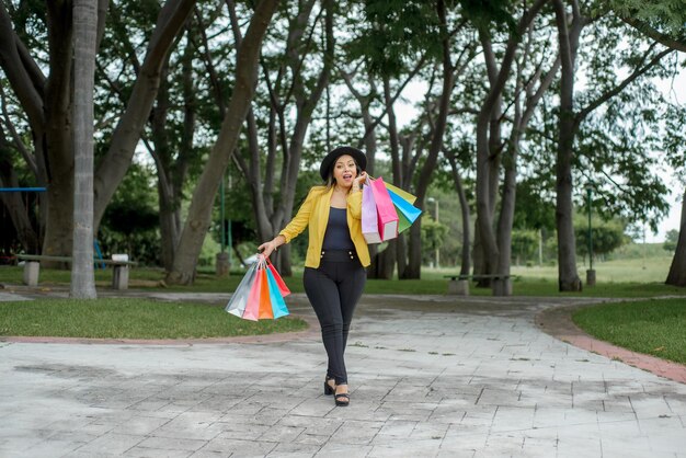 Mujer vistiendo chaqueta amarilla caminando en un jardín con bolsas de diferentes colores