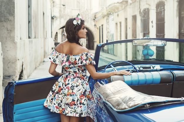 Mujer vistiendo un hermoso vestido y coche convertible retro en la ciudad de La Habana.