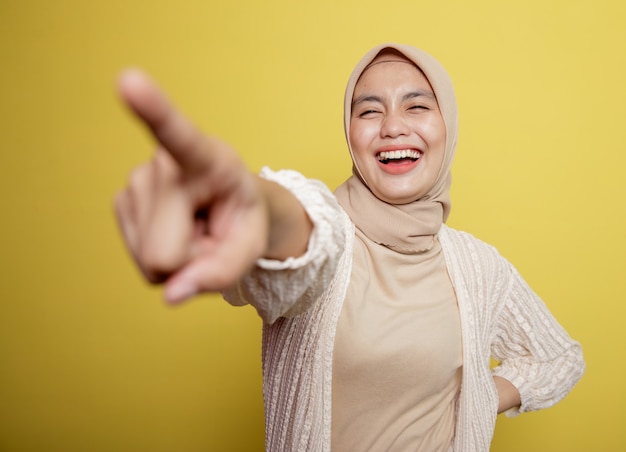 Mujer vistiendo hijab apunta a alguien aislado en una pared amarilla