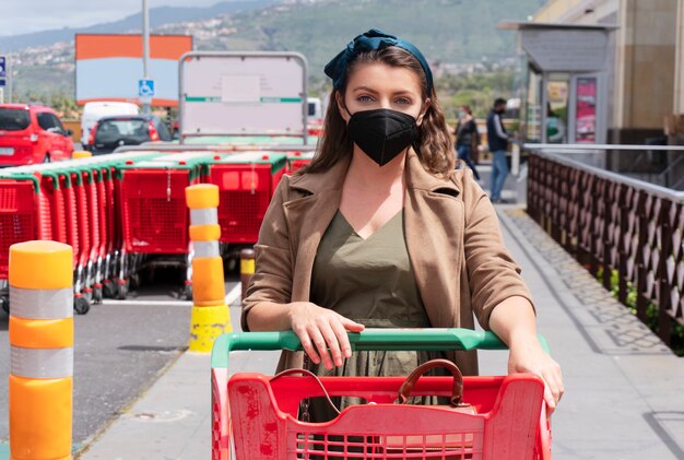 Mujer vistiendo máscara protectora con carrito de compras al aire libre del centro comercial