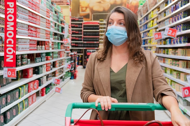 Mujer vistiendo máscara protectora con carrito de compras de cerca, comprobando la descripción del producto