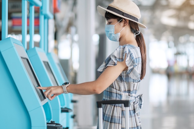 Mujer vistiendo mascarilla médica y usando la máquina de auto check-in en la terminal del aeropuerto