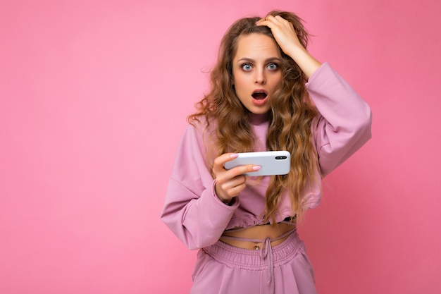 mujer vistiendo ropa casual elegante que se encuentran aisladas sobre la pared con espacio de copia sosteniendo y usando el teléfono móvil.