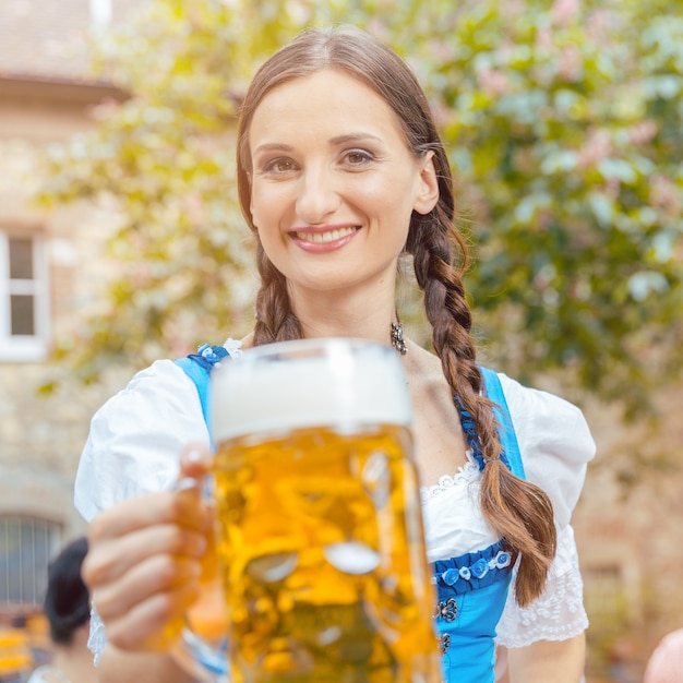 Mujer vistiendo traje de Dirndl está bebiendo cerveza en un jardín de cerveza bávaro