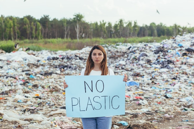 Mujer voluntaria hace piquetes en un vertedero con un cartel sin plástico, activista lucha contra la contaminación ambiental