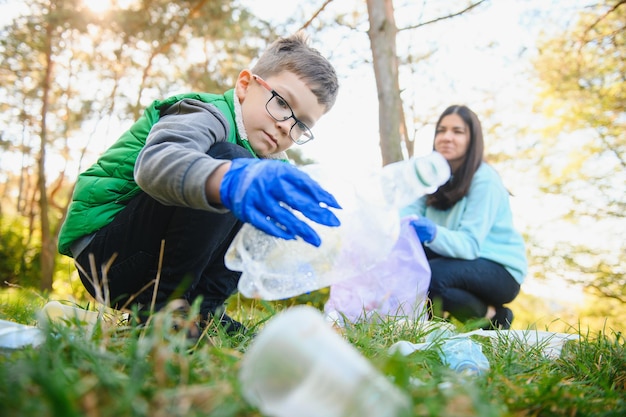 Foto mujer voluntaria y niño recogiendo la basura plástica y colocándola en una bolsa de basura biodegradable al aire libre. ecología, reciclaje y protección del concepto de naturaleza. protección del medio ambiente.