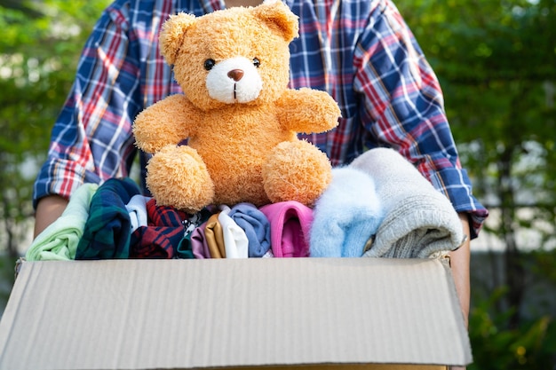 Mujer voluntaria proporciona caja de donación de ropa con ropa usada y muñeca