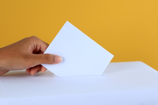 Mujer votando cerca de la urna de votación en un fondo de color amarillo