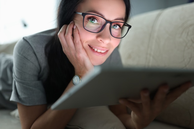 La mujer yace en el sofá con el concepto de trabajo remoto de tableta incluido