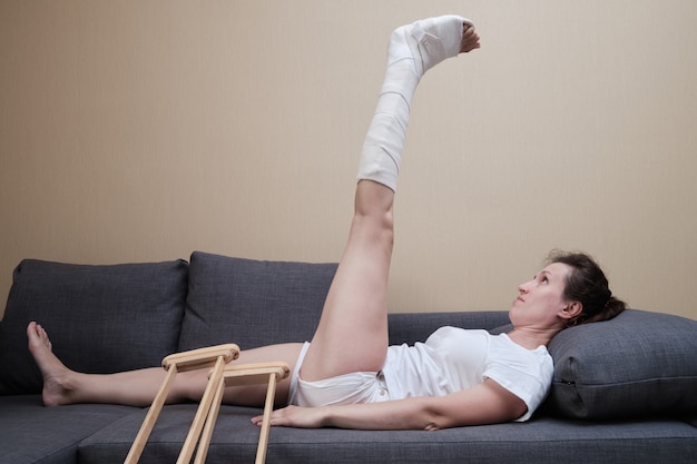Una mujer con un yeso en la pierna está haciendo ejercicios físicos. Rehabilitación después de una lesión.