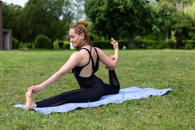 Mujer yogui con rastas practicando King Pigeon Eka Pada Rajakapotasana pose en estera de yoga