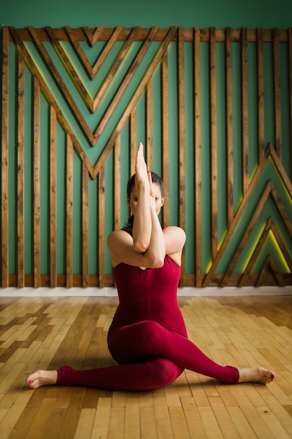 Mujer yogui en ropa deportiva marrón se sienta en la asana Vatayanasana en la habitación