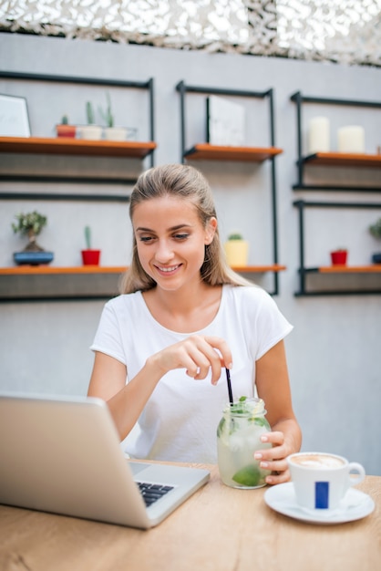 Mujer de Yooung en el café que bebe limonada y que trabaja en la computadora portátil.