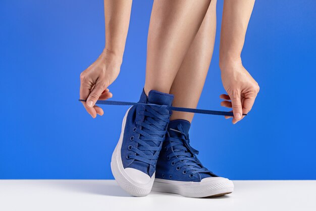 Una mujer en zapatillas azules está atando sus cordones