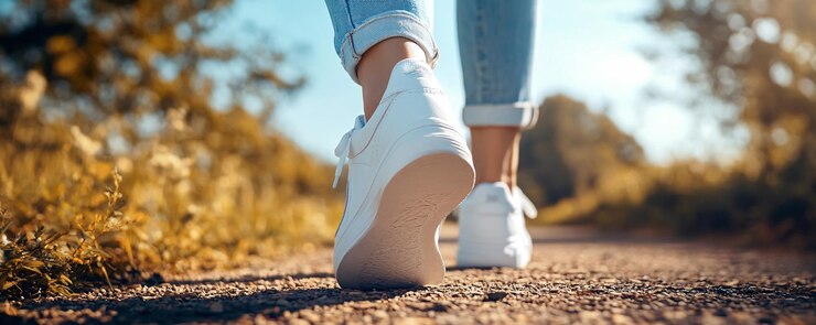 Mujer con zapatillas blancas alejándose de la cámara en un camino de tierra soleado