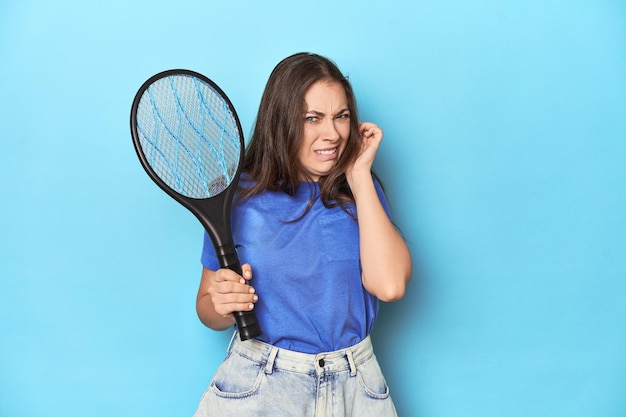 Foto mujer con un zapper de insectos eléctrico en un fondo azul cubriendo las orejas con las manos