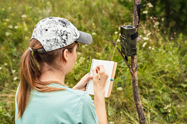 Foto mujer zoóloga escribiendo datos de la cámara trampa en el bloc de notas observando animales silvestres día de la vida silvestre