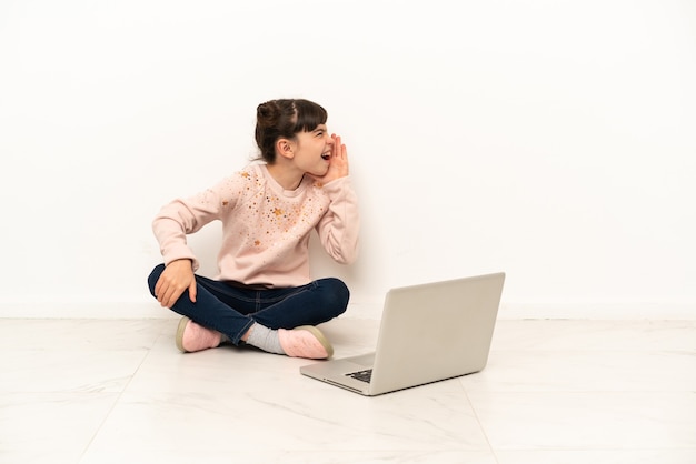 Mujercita con una computadora portátil sentada en el suelo gritando con la boca abierta hacia un lado