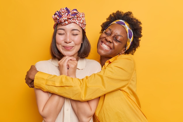 las mujeres se abrazan tienen una relación amistosa, felices de pasar el tiempo libre juntas, usan ropa elegante, posan en amarillo vivo