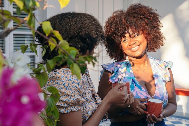 Mujeres afro bebiendo café juntas afuera divirtiéndose y hablando