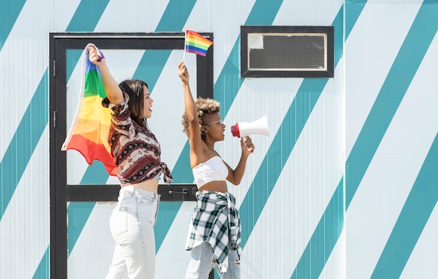 Mujeres, afro y caucásicas, con bandera del orgullo gay y megáfono, se manifiestan por la igualdad