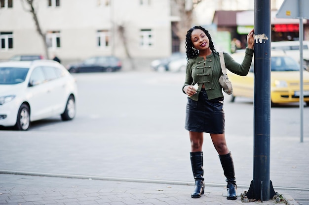 Mujeres afroamericanas de moda con estilo en suéter verde y falda negra posadas al aire libre con teléfono móvil