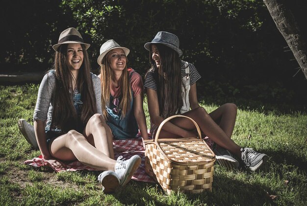 Mujeres alegres con una canasta de picnic mientras están sentadas en el parque