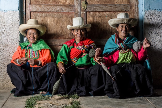 Mujeres andinas latinoamericanas sentadas en la acera haciendo hilo y sonriendo por la noche
