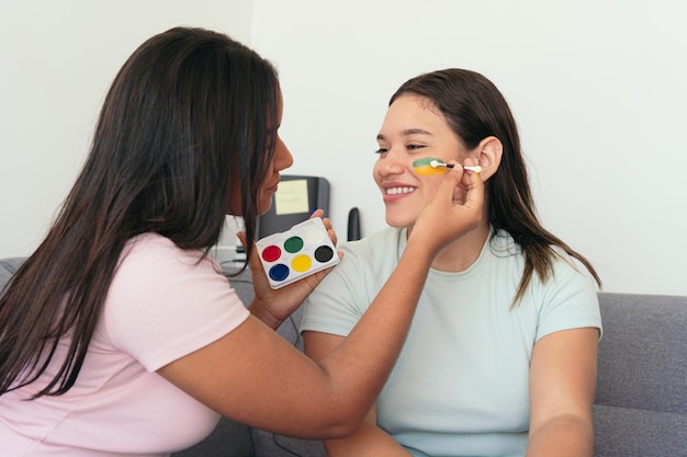 Mujeres aplicando pintura facial en la mejilla de la mujer mientras ven un partido de fútbol en casa