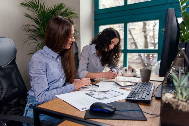 Mujeres arquitectas guapas con camisas azules que trabajan con paleta de colores para elegir el diseño y los colores en la oficina.