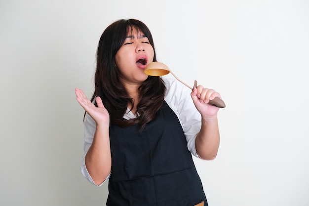 Mujeres asiáticas adultas con delantal que muestran emoción cantando con cucharón en la cocina