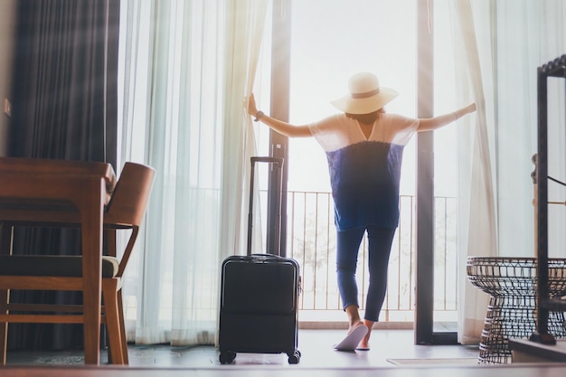 Las mujeres asiáticas se alojan en una habitación de hotel con equipajeAbra la cortina y la puerta de la habitación mirando hacia el exteriorConcepto de viaje en vacacionesTono vintage