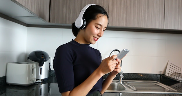 Las mujeres asiáticas con auriculares y escuchando música en la cocina de casa