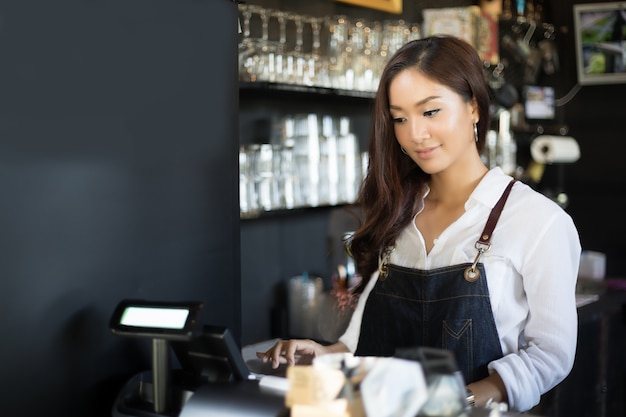 Mujeres asiáticas Barista sonriendo y usando la máquina de café en el mostrador de la cafetería