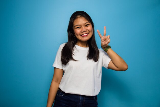 Las mujeres asiáticas con camiseta blanca con fondo azul aislado mostrando el signo de la paz y sonriendo