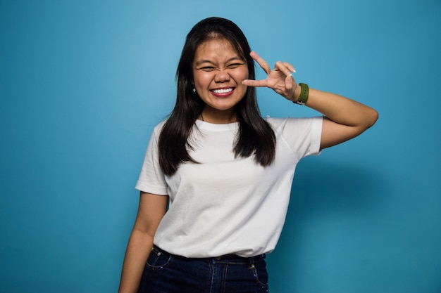 Las mujeres asiáticas con camiseta blanca con fondo azul aislado mostrando el signo de la paz y sonriendo